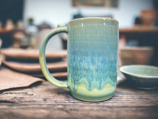 a green and blue colored mug in a pottery studio